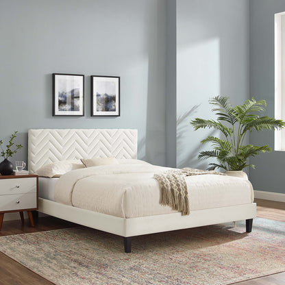 White upholstered platform bed with chevron tufted headboard, beige bedding, white nightstands, potted palm, blue-gray walls.