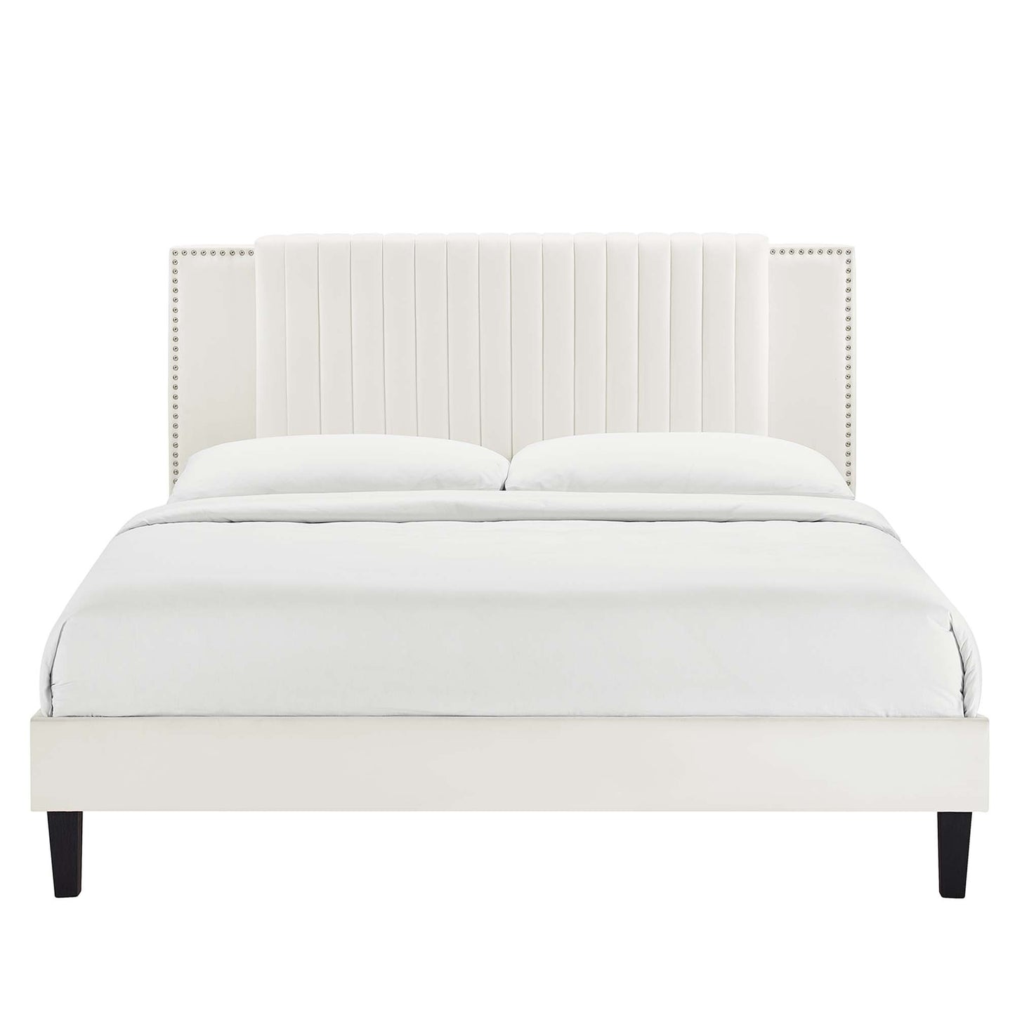 White upholstered platform bed with tall vertical-channel headboard, nailhead trim, dark legs, dressed in white bedding.
