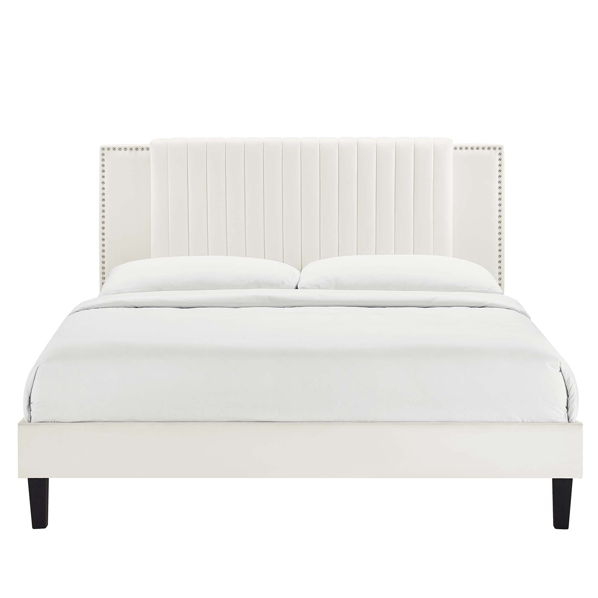 White upholstered platform bed with tall vertical-channel headboard, nailhead trim, dark legs, dressed in white bedding.