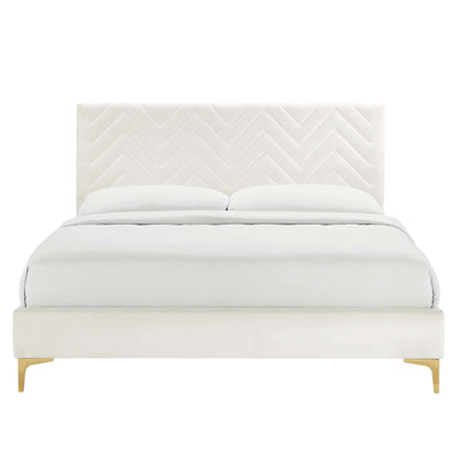 White upholstered full platform bed with chevron-tufted headboard, white bedding, and white platform with wooden legs.