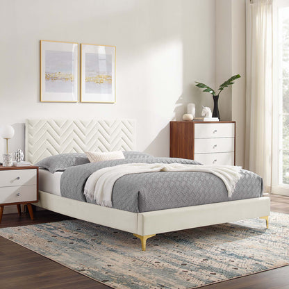 Cream upholstered platform bed with chevron-tufted headboard, gray bedding, gold legs; wood nightstands and dresser.