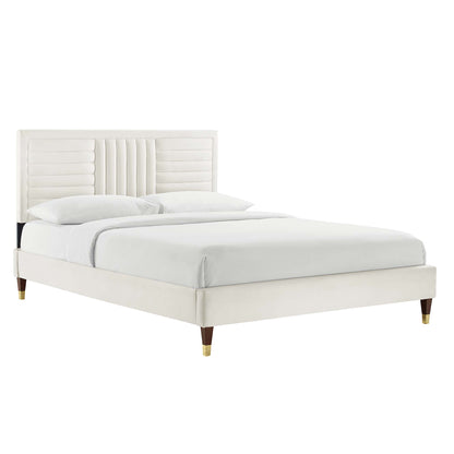 White upholstered bed with a vertically tufted headboard & low-profile platform frame & brass-capped wooden legs.