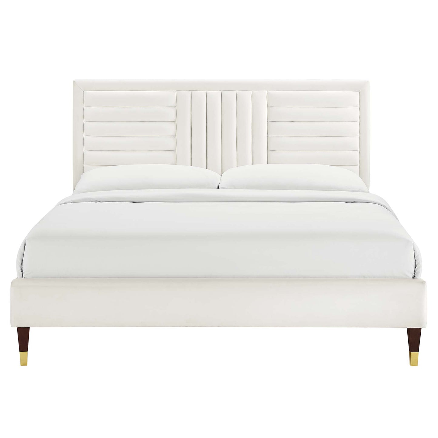 White upholstered bed with tall headboard featuring vertical channel tufting, white bedding, and dark legs with brass caps.
