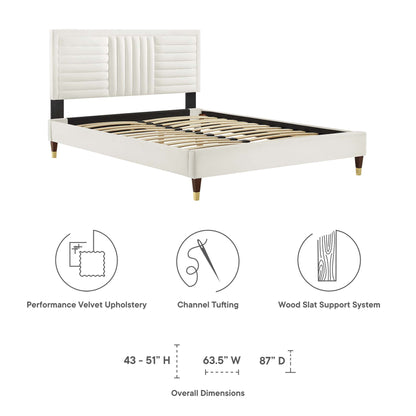 White velvet-upholstered platform bed with tufted headboard, black accents, tapered wood legs with brass tips, slatted base.