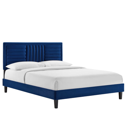 Blue velvet platform bed with tall, tufted headboard featuring vertical channels, white linens, tapered legs.