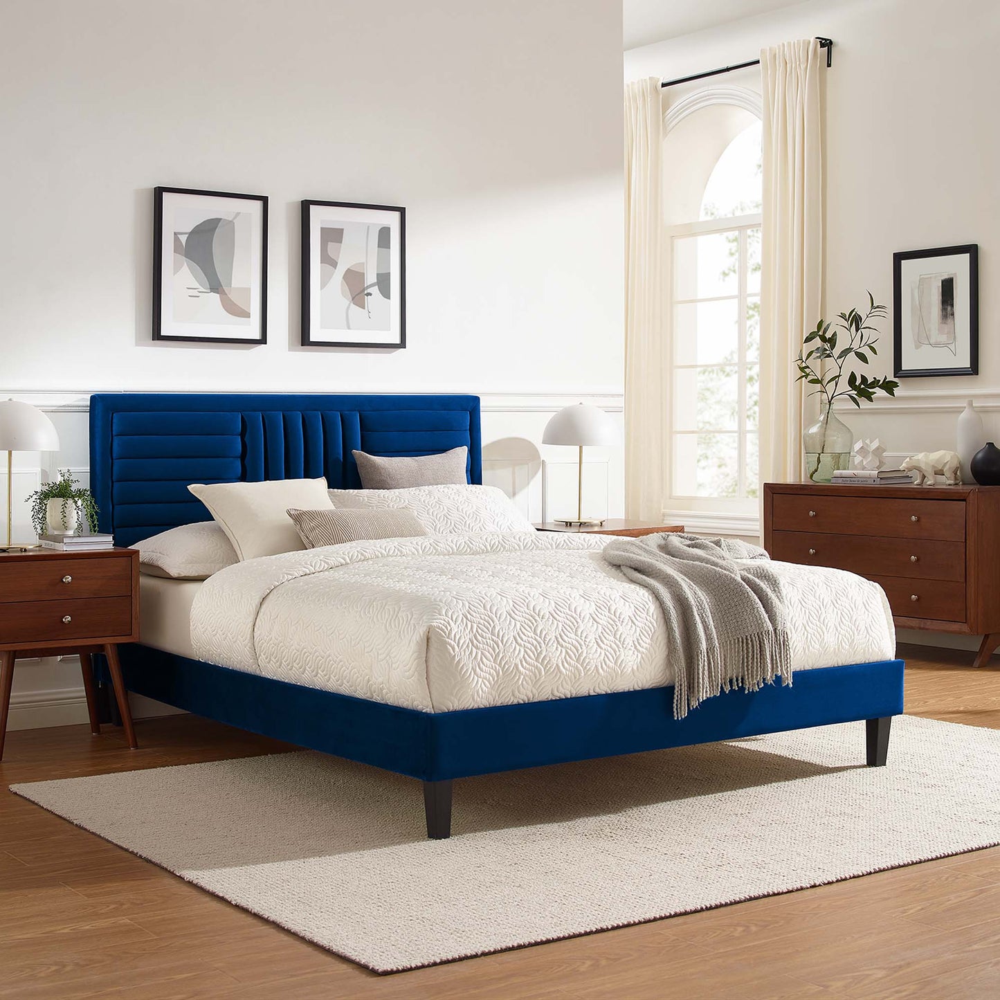 Navy blue upholstered platform bed with tufted headboard, white quilt, gray throw, wooden nightstands, beige rug.