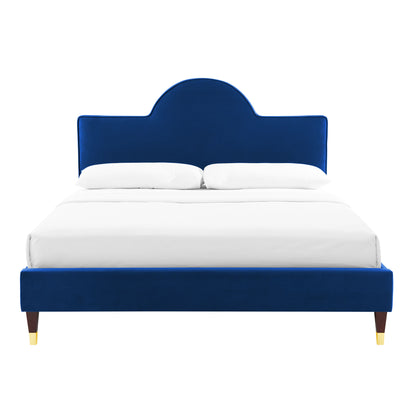 Navy blue velvet upholstered bed with a rounded arch headboard, white linens, and dark wood legs with gold tips.