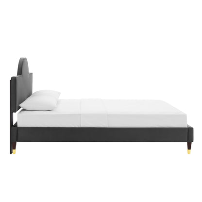 Dark charcoal upholstered platform bed with tall curved headboard, white sheets and pillows, gold-tipped legs.