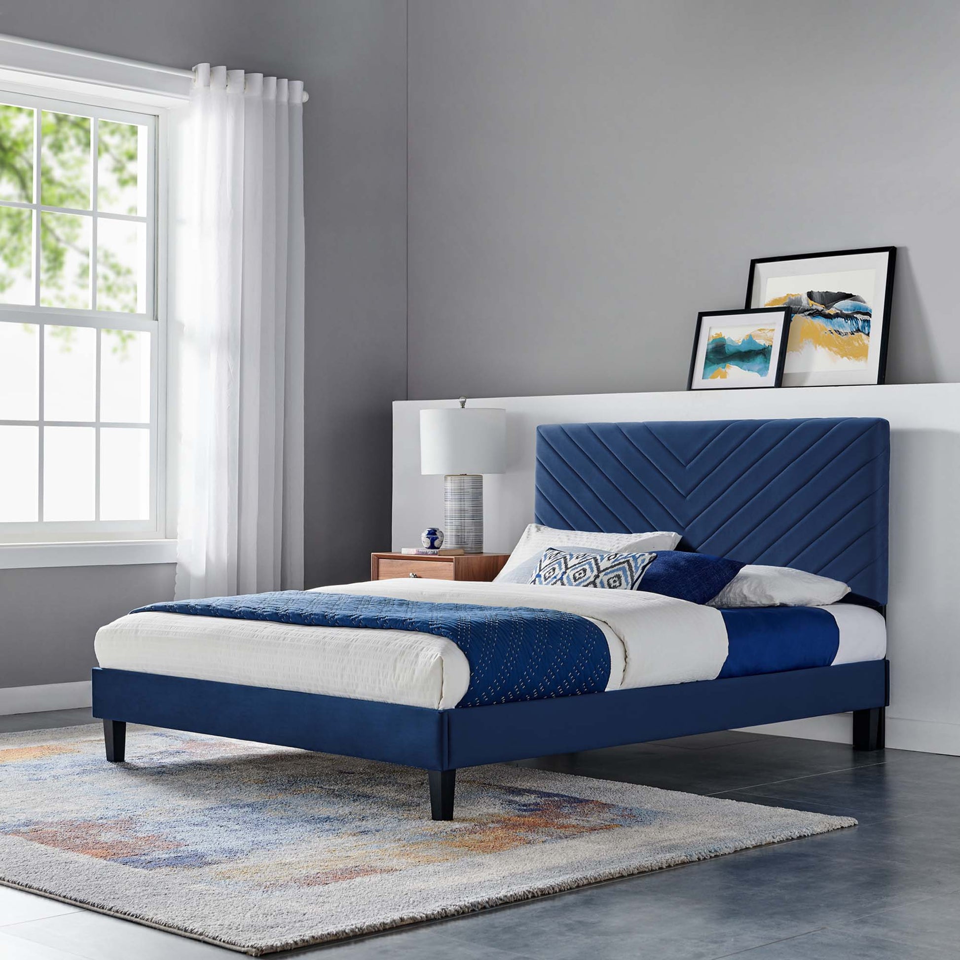 Blue upholstered platform bed with chevron headboard, black tapered legs, white and blue bedding in a modern gray bedroom.
