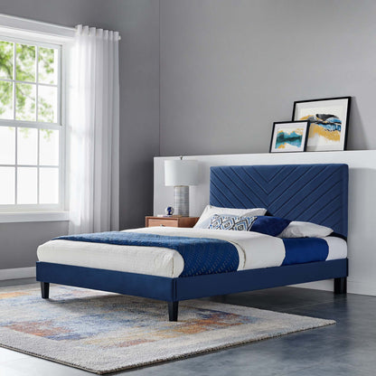 Blue upholstered platform bed with chevron headboard, black tapered legs, white and blue bedding in a modern gray bedroom.