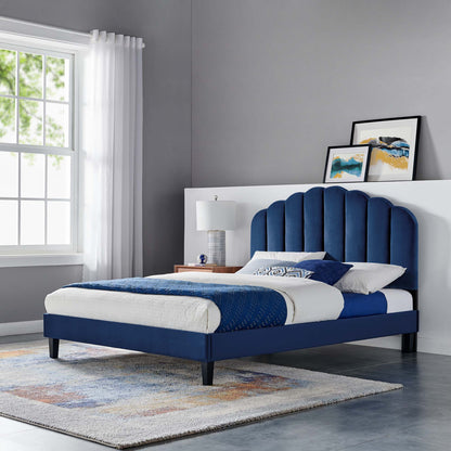 Navy blue upholstered platform bed with curved, tufted arched headboard, white/blue bedding, dark legs, modern bedroom scene.