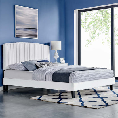 White platform bed with tall upholstered headboard in blue room, striped gray-blue bedding, modern lamp, rug, large window.