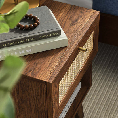 Walnut wood nightstand with a woven cane drawer front and brass knob; books and a beaded bracelet on top.