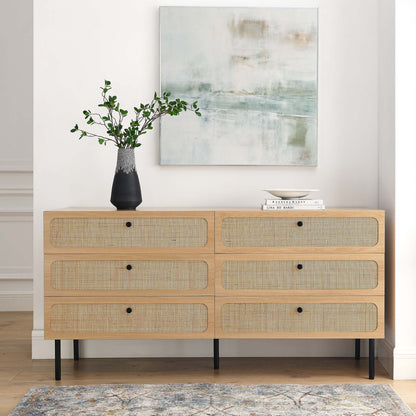 Oak 6-drawer dresser with woven-rattan fronts, black knobs and slim black legs, greenery vase, books, and abstract art.