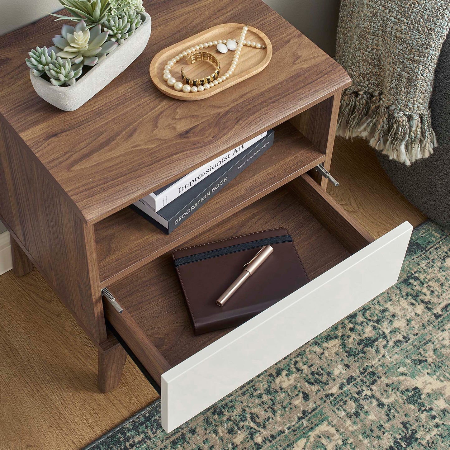 Walnut finish wood nightstand with white front drawer, open shelf and lower drawer; succulent and jewelry on top.