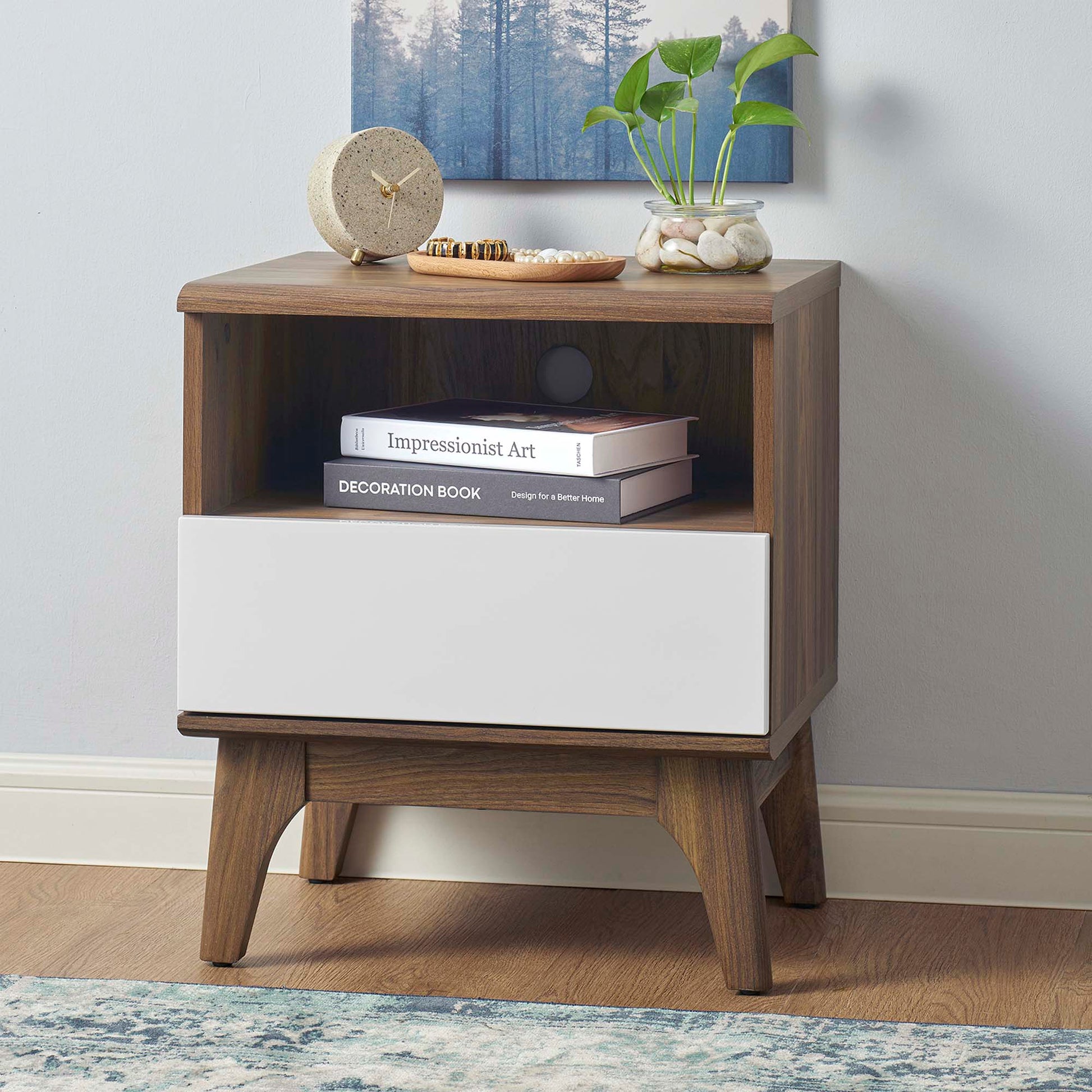 Walnut mid-century nightstand with open shelf and white front drawer, angled legs; top decor with clock and plant.