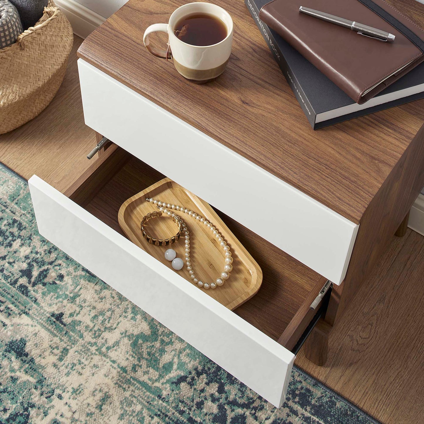 Walnut nightstand with white drawers, open lower drawer with pearl necklace and jewelry tray; coffee cup and books on top.