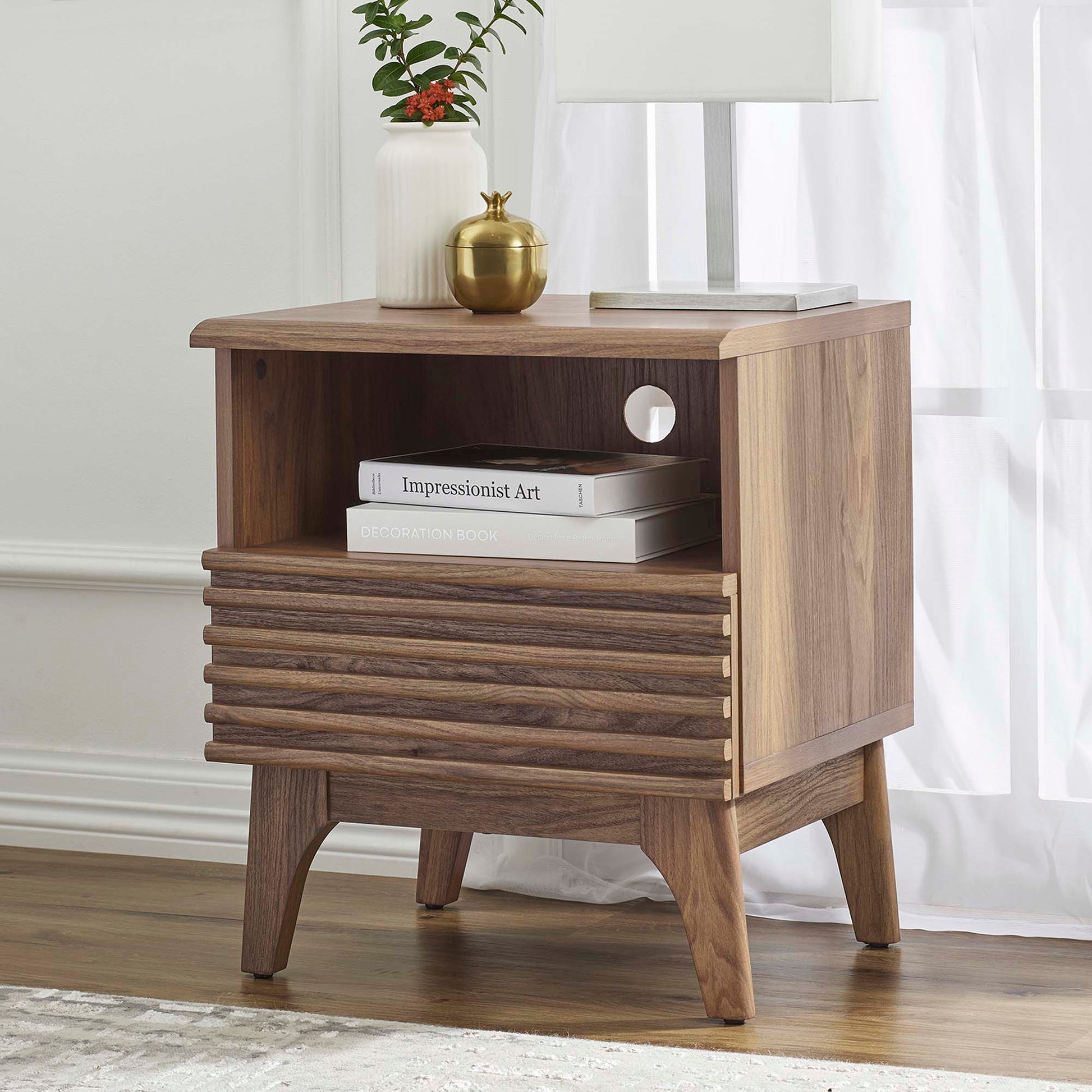 Brown mid-century nightstand with open shelf, slatted drawer, and tapered legs; topped with lamp and decorative vase.