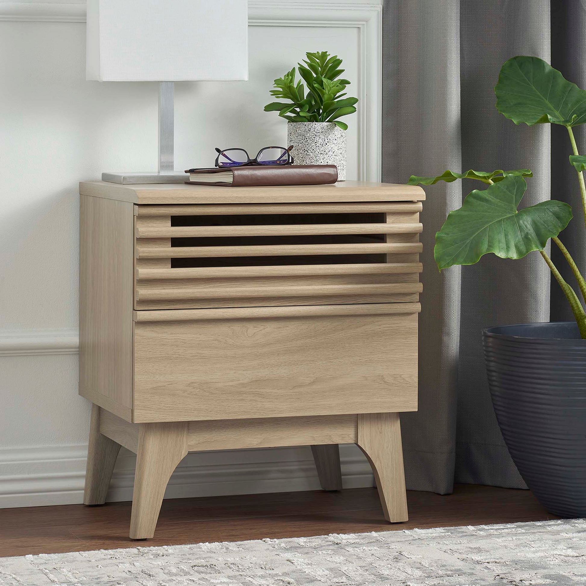 Brown nightstand with a vented slatted drawer and curved legs; lamp, plant, glasses, and book on top.