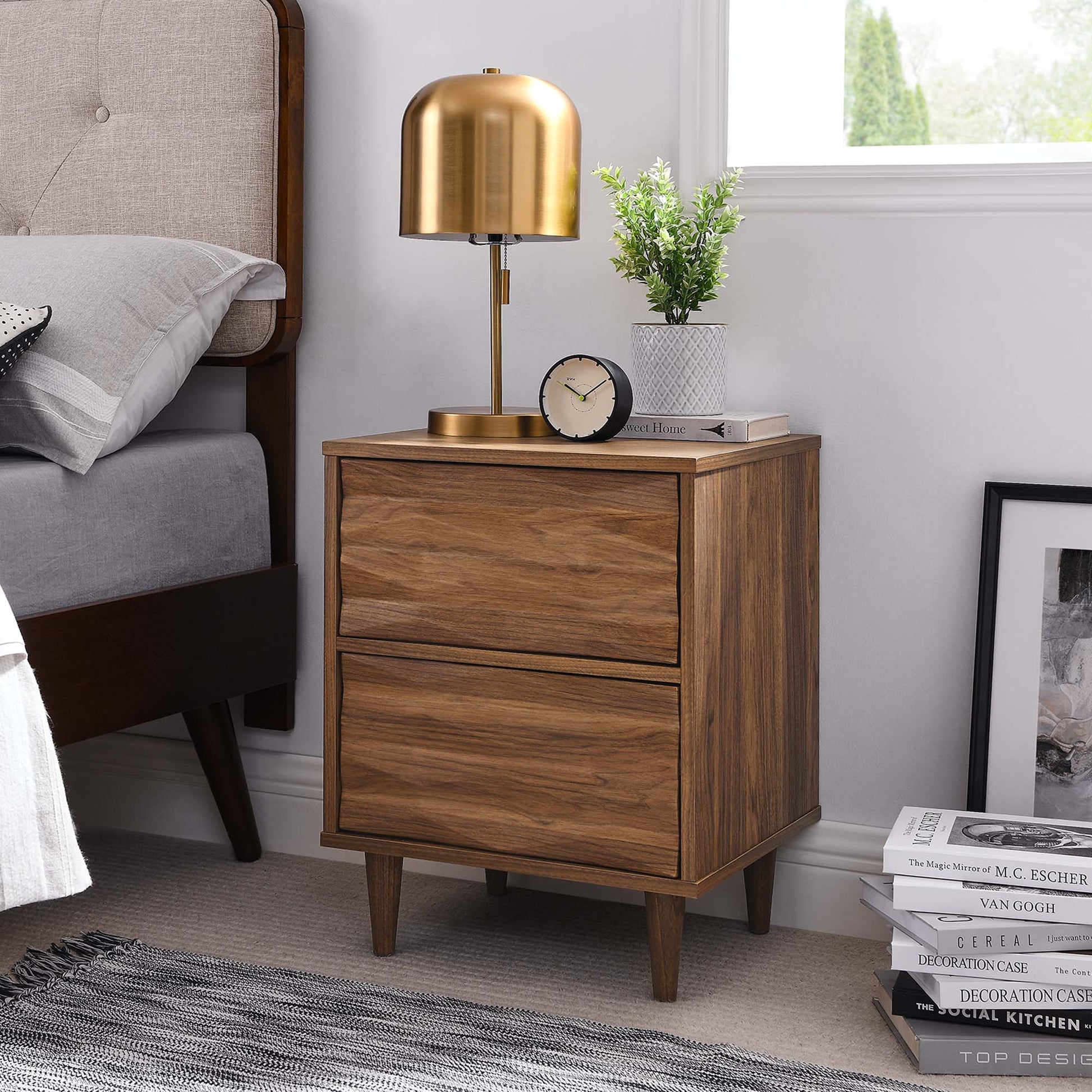 Walnut mid-century two-drawer nightstand with tapered legs, brass lamp, clock, and potted plant on top.