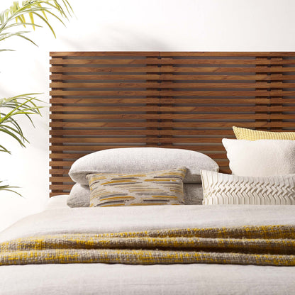 Brown, wall-mounted queen headboard with a wooden slat design; neutral gray linens, striped and chevron pillows, mustard accents; plant nearby.