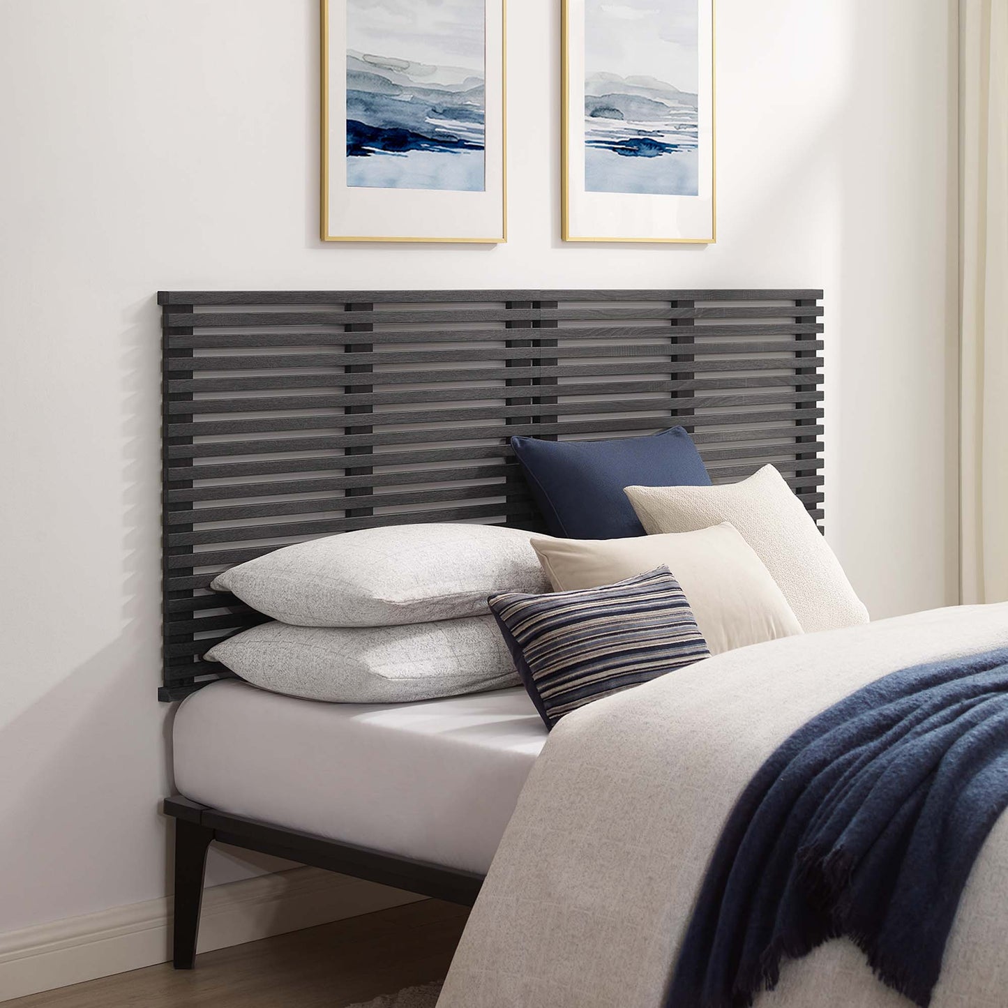 Dark gray horizontal slat headboard with light bedding, navy throw, beige and striped pillows; blue framed art above.