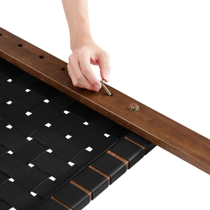 A hand inserts a brass pin into a dark wood headboard frame around a black woven surface with metal fasteners.