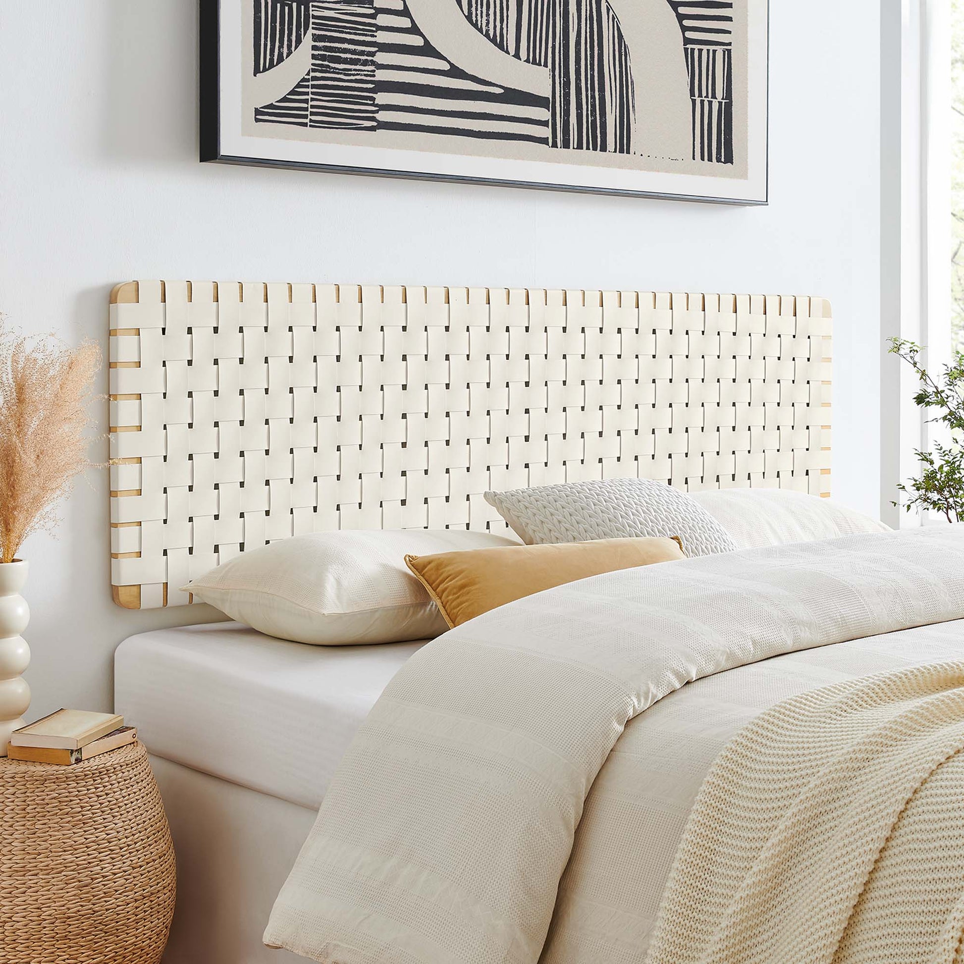 Natural beige vegan leather headboard on a white bed with cream linens; dried pampas grass vase beside bed and abstract art above.