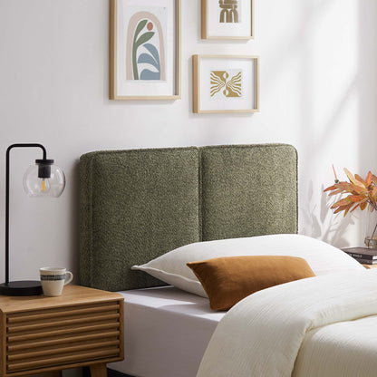 Cozy bedroom with olive-green upholstered headboard, white linens, rust pillow, wooden nightstand, black lamp, framed art.