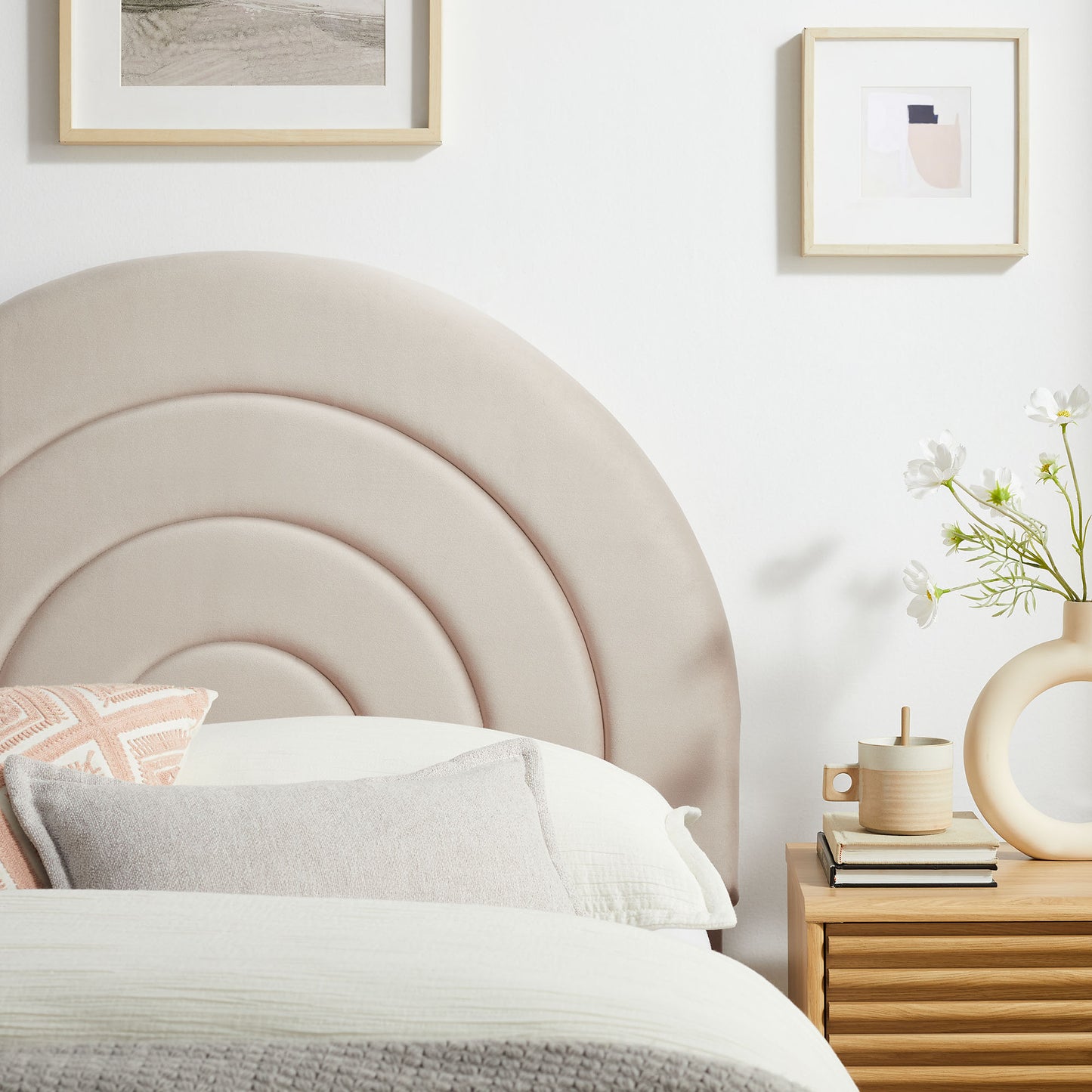 Soft taupe upholstered headboard with concentric arcs; white bedding, peach pillow, wooden nightstand, vase.