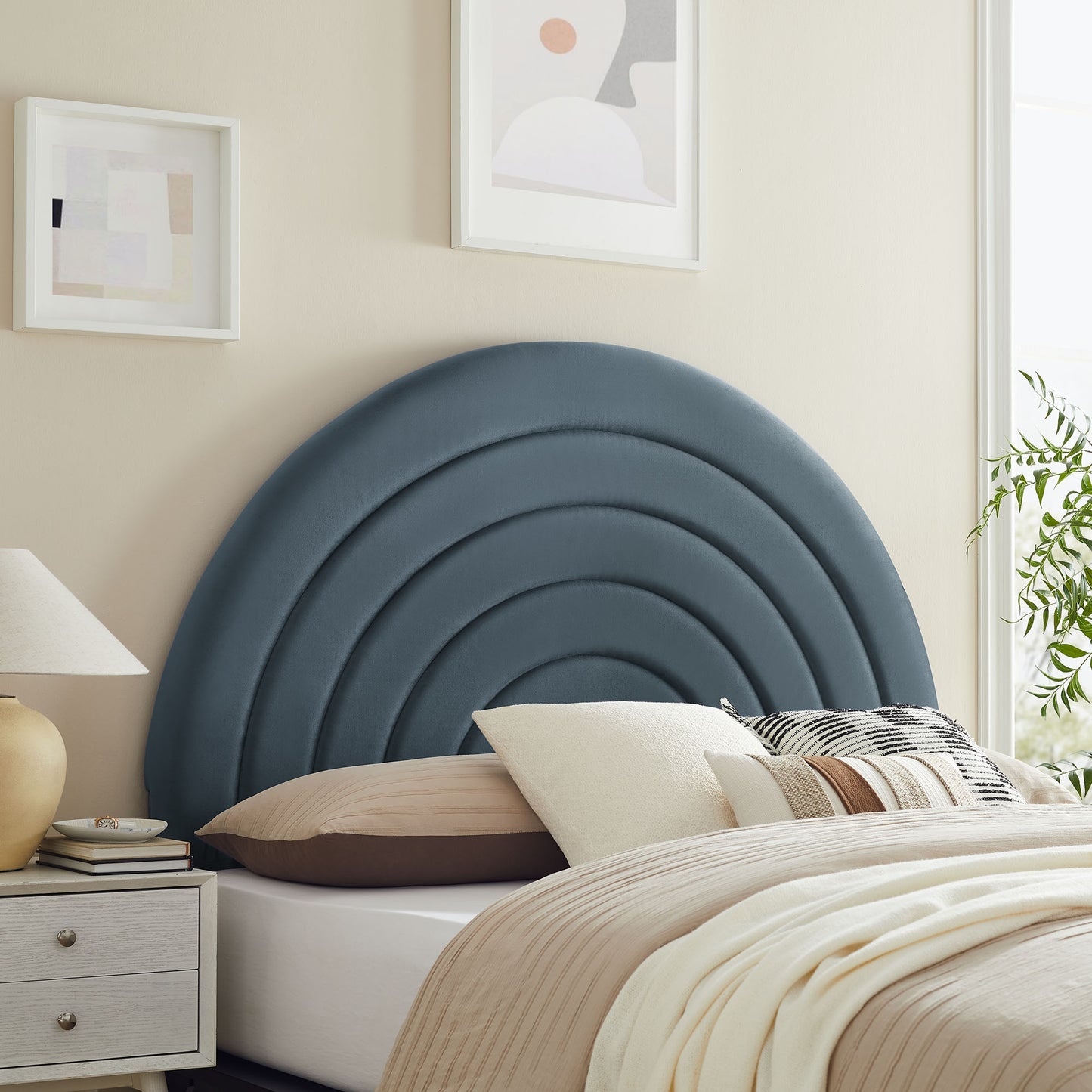 Blue upholstered concentric arc headboard with beige bed and cream bedding; nightstand, lamp, abstract wall art