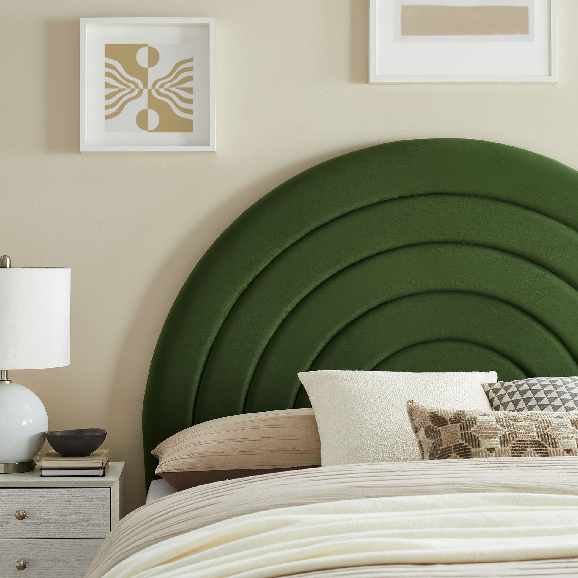 Deep green curved upholstered headboard with layered arches, beige bedding, white nightstand, lamp, and neutral wall art.