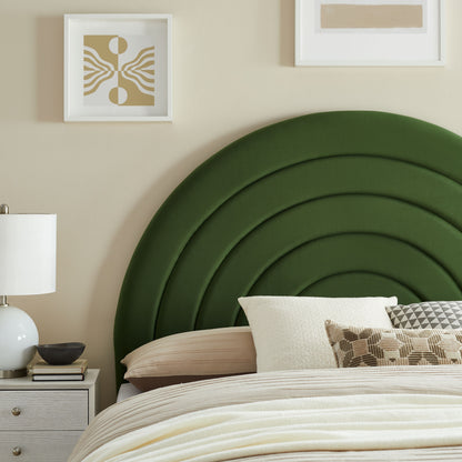 Deep green curved upholstered headboard with layered arches, beige bedding, white nightstand, lamp, and neutral wall art.