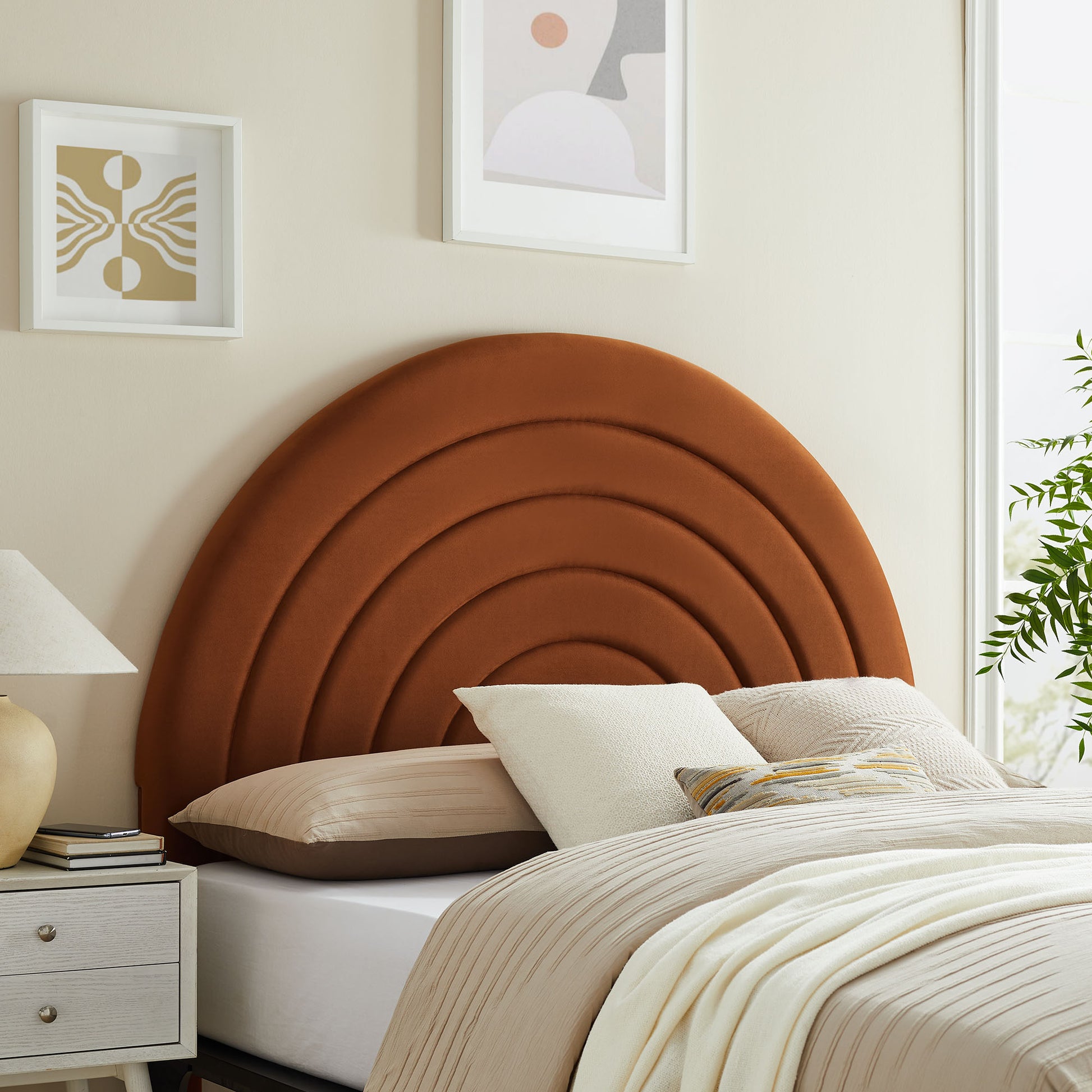 Arched rust-orange upholstered queen headboard in a bedroom setup with cream bedding, a white nightstand and abstract art.