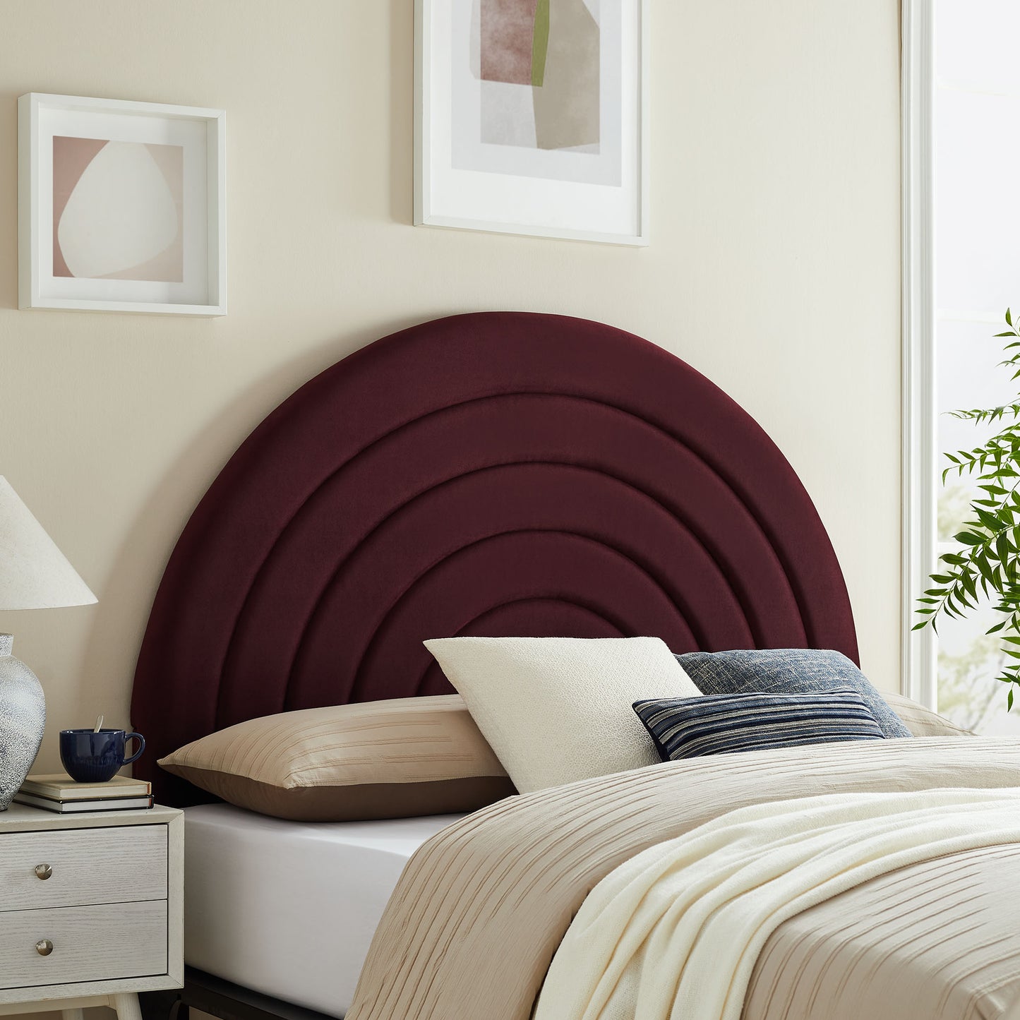 Maroon velvet arched headboard with concentric circles, beige bedding, white and blue striped pillows beside nightstand.