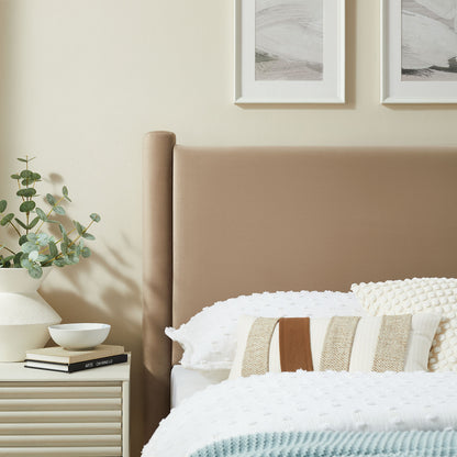 Taupe upholstered twin headboard with white knit bedding, striped pillows, and a cream nightstand holding a plant in a white vase.