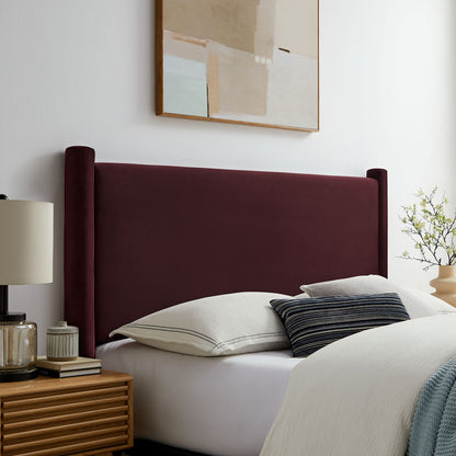 Purple velvet full headboard on a bed with white linens and a striped pillow; wooden nightstand and beige lamp in a modern bedroom.