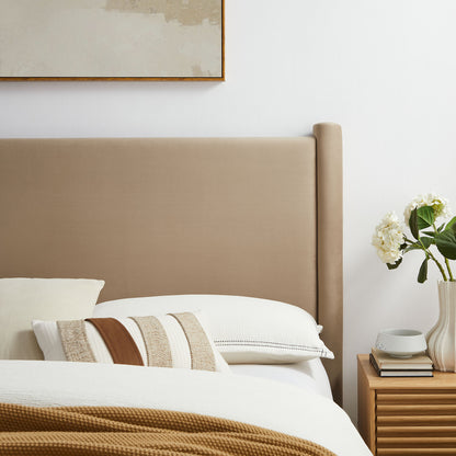 Taupe upholstered king headboard with white linens, striped beige cushions, and a tan throw; wooden nightstand with vase of flowers.