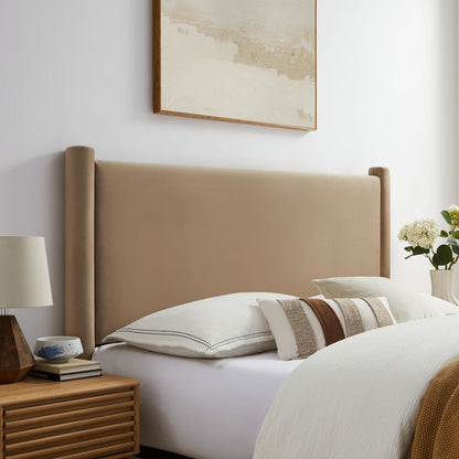 Taupe upholstered king headboard with tall profile; white linens and decorative pillows; wooden nightstand, lamp, and flowers.