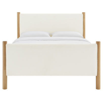 Ivory bouclé upholstered platform bed with light oak posts, padded headboard & footboard, white bedding.