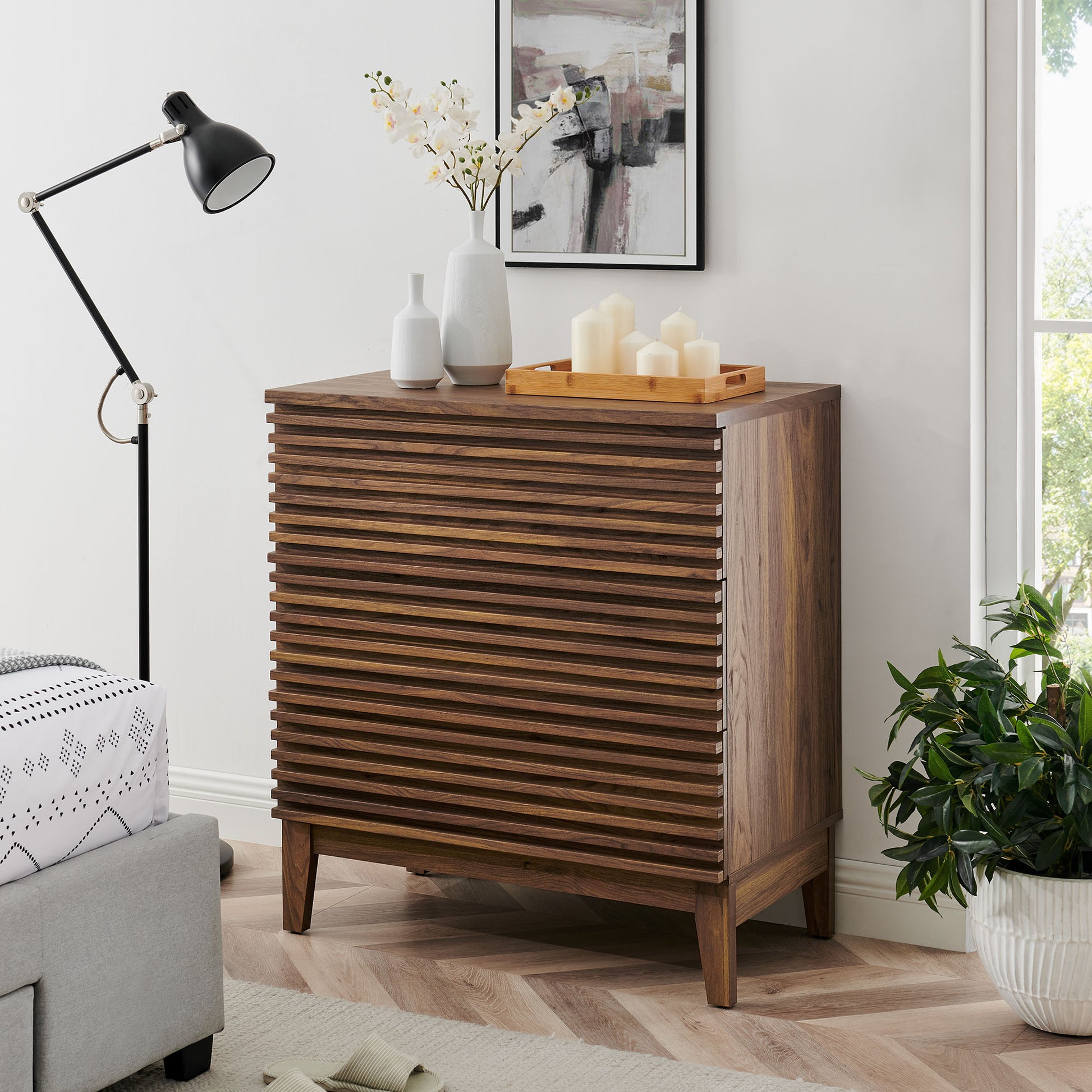 Walnut wood 3-drawer nightstand with mid-century legs, topped with vases & candles in a modern living room.