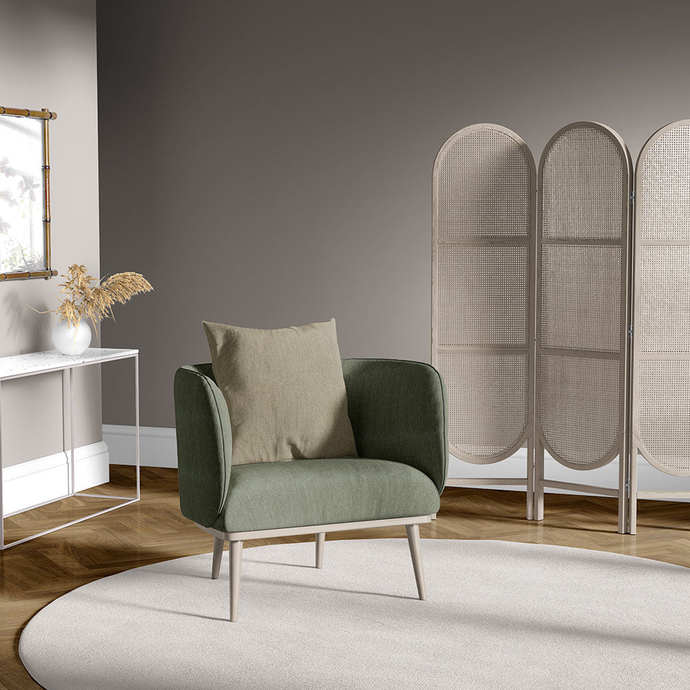 Olive-green curved armchair with beige cushion, light wood legs, set in a modern living room with a woven folding screen.
