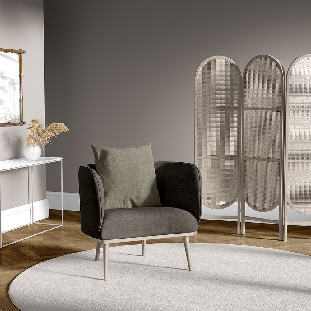 Truffle solid fabric upholstered armchair with pale wood legs and an olive cushion in a neutral living room with a round cream rug.