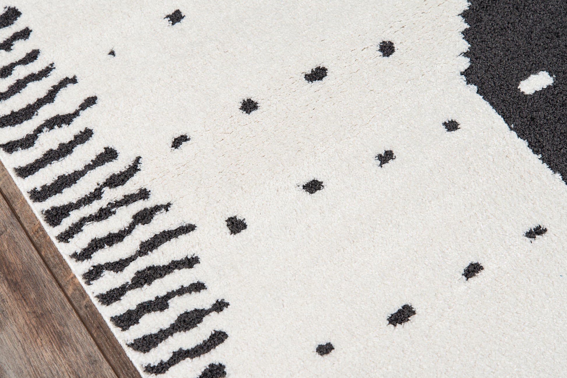 Cream shag rug with scattered black dots and a black fringe trim along the left edge.