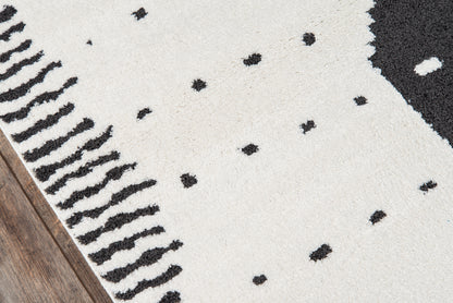 Cream shag rug with scattered black dots and a black fringe trim along the left edge.