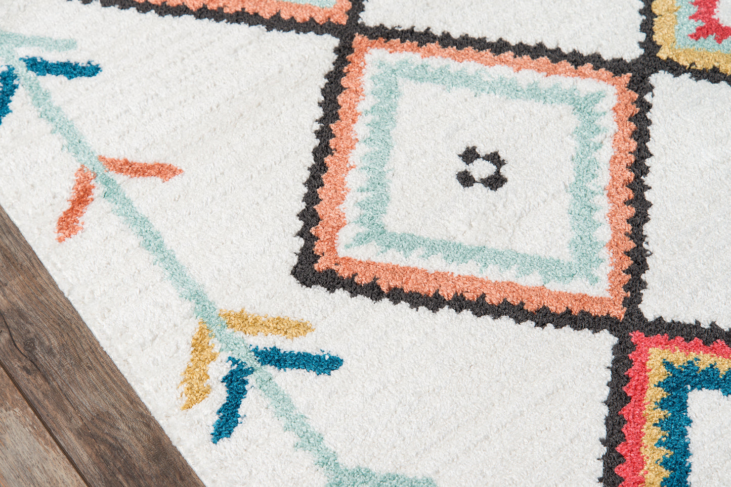 Shaggy white area rug with multicolored geometric squares in teal, peach, black & coral on a wooden floor.