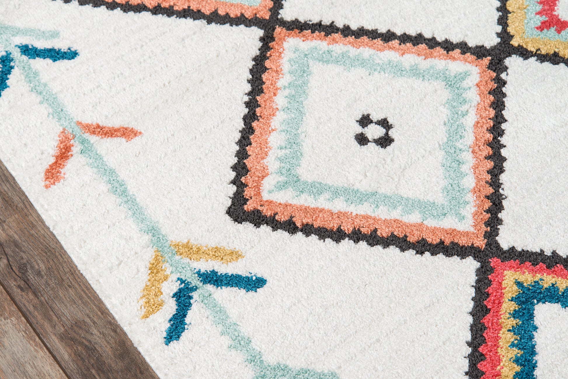 Shaggy white area rug with multicolored geometric squares in teal, peach, black & coral on a wooden floor.