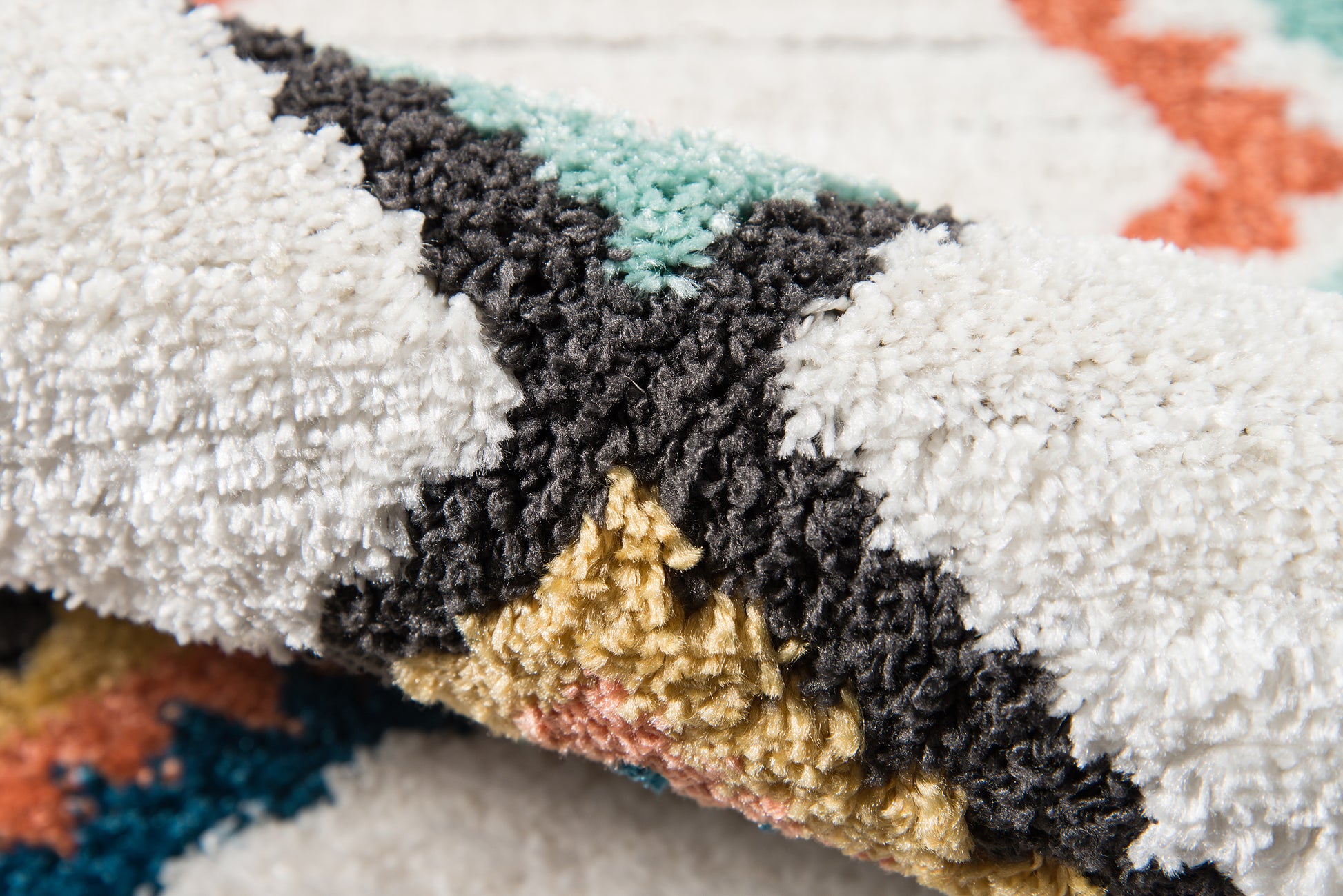 Close-up of a multicolor fluffy shag rug with white, black, teal, gold and coral geometric triangles.