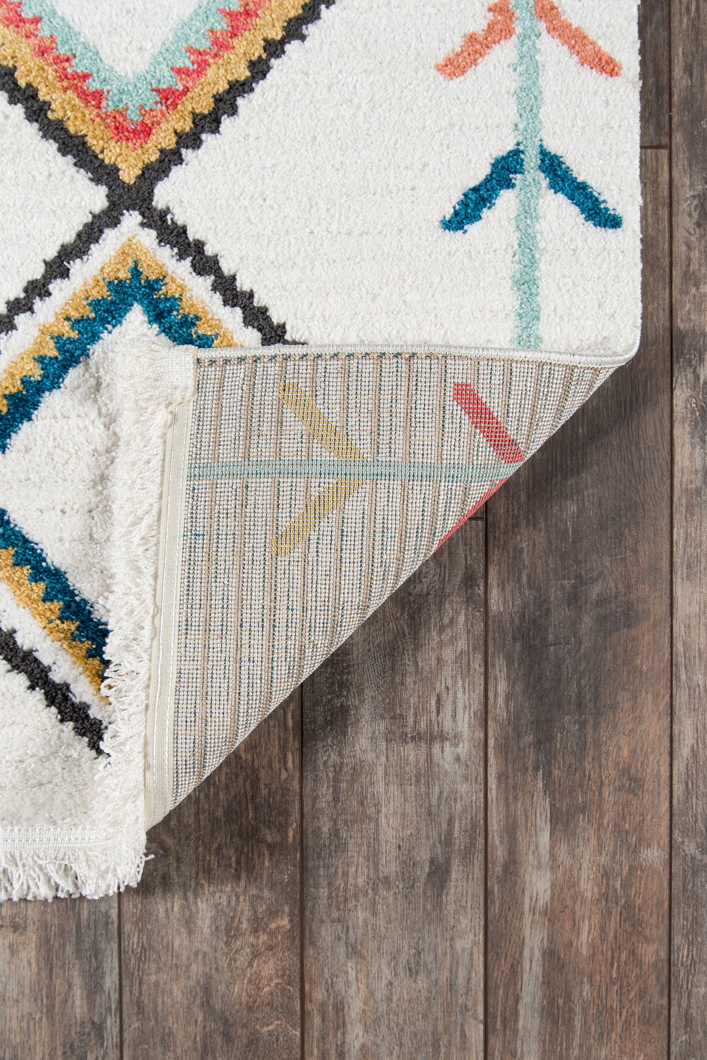 Moroccan-inspired rug with ivory base, teal, coral, yellow diamonds; fringed edge, folded corner reveals striped back.
