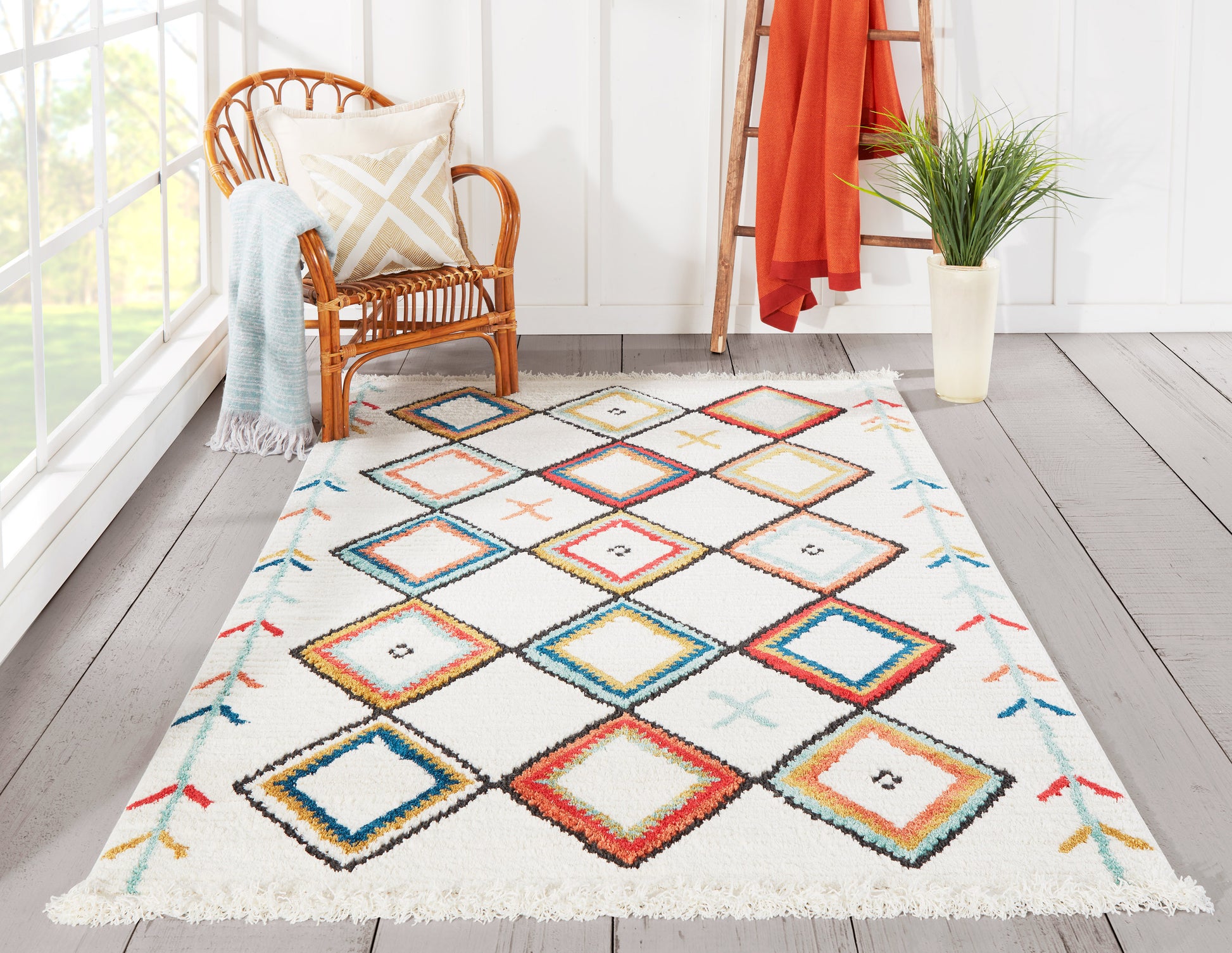 Multicolor diamond-pattern rug with fringe edges in a sunlit nook beside a wicker chair, blue throw, orange ladder.
